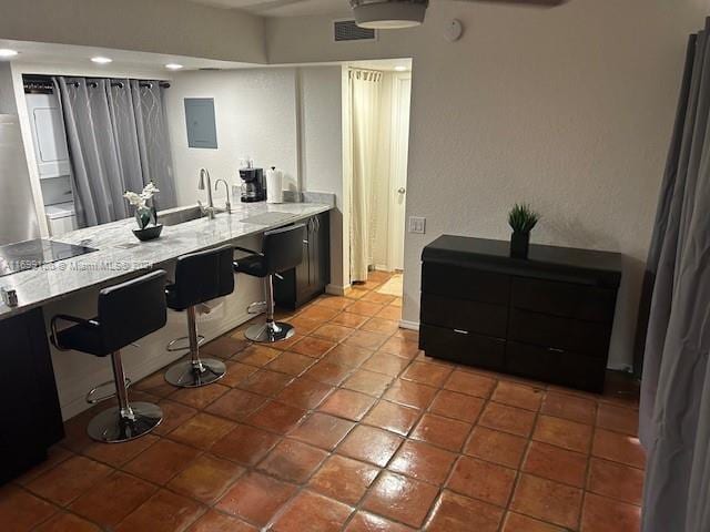 interior space featuring tile patterned floors, electric panel, light stone countertops, and a kitchen bar