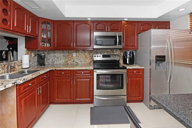 kitchen with light tile patterned flooring, sink, appliances with stainless steel finishes, light stone countertops, and decorative backsplash