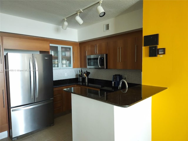 kitchen with dark stone countertops, a textured ceiling, appliances with stainless steel finishes, tasteful backsplash, and kitchen peninsula