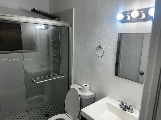 full bath with vanity, a textured wall, a stall shower, and toilet