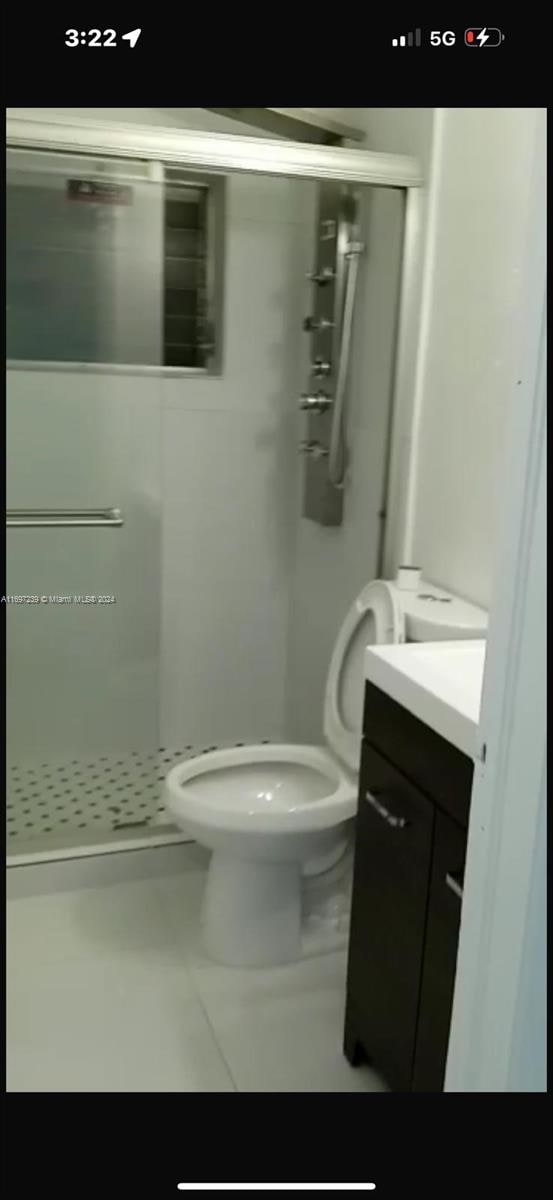 bathroom featuring tile patterned floors, vanity, a shower with shower door, and toilet