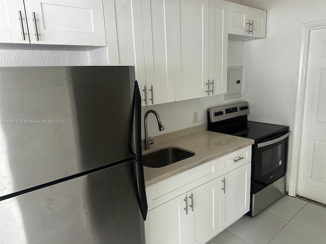 kitchen with freestanding refrigerator, light tile patterned flooring, stainless steel electric stove, white cabinets, and a sink