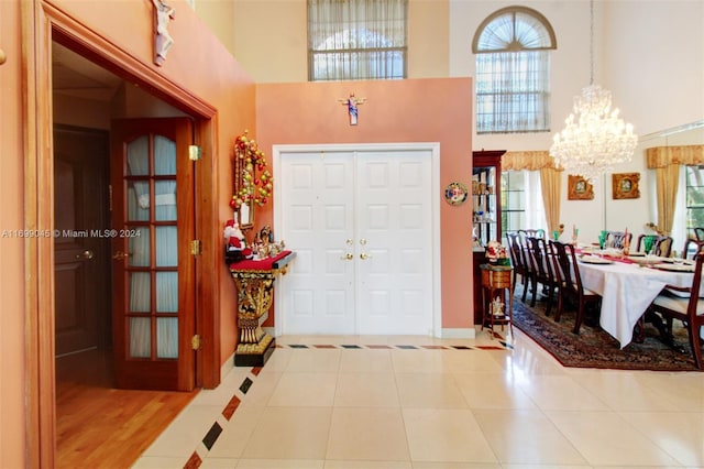 tiled foyer entrance featuring a healthy amount of sunlight, a high ceiling, and an inviting chandelier