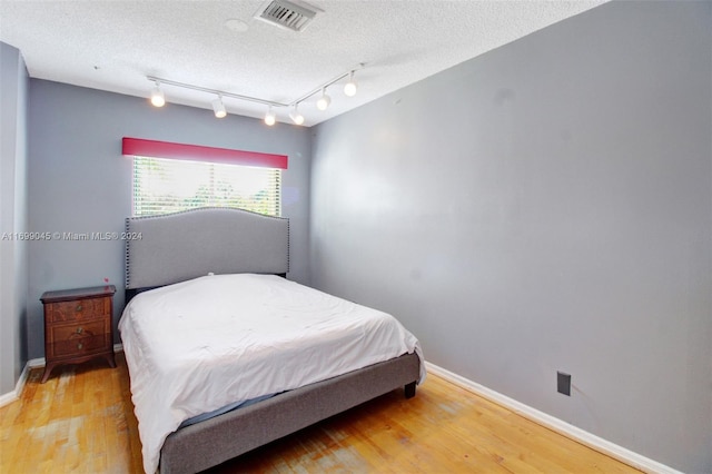 bedroom featuring a textured ceiling, hardwood / wood-style floors, and track lighting