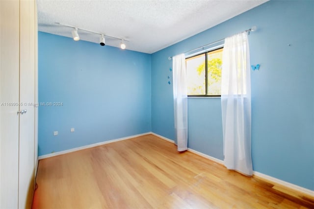 unfurnished room featuring rail lighting, wood-type flooring, and a textured ceiling