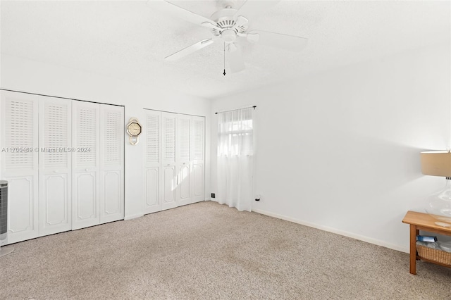 unfurnished bedroom featuring a textured ceiling, ceiling fan, light colored carpet, and two closets