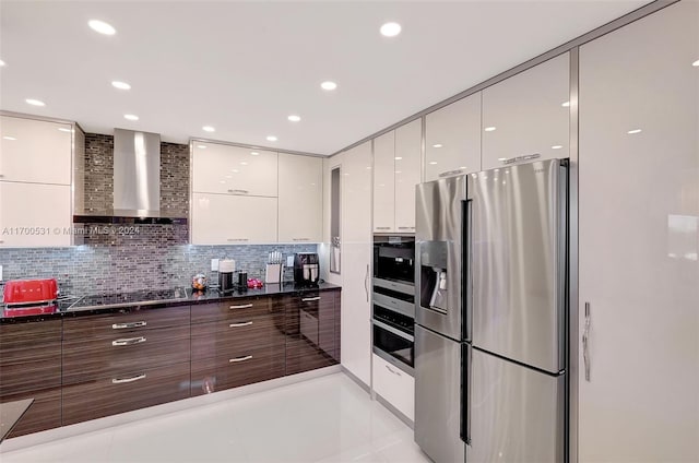 kitchen with white cabinetry, wall chimney exhaust hood, stainless steel appliances, dark stone counters, and light tile patterned floors