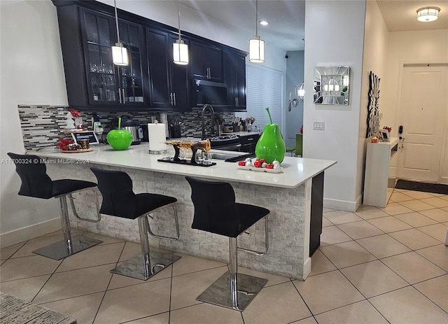 kitchen featuring hanging light fixtures, light tile patterned floors, tasteful backsplash, kitchen peninsula, and a breakfast bar area