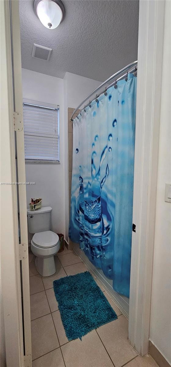 bathroom featuring shower / bathtub combination with curtain, toilet, tile patterned flooring, and a textured ceiling