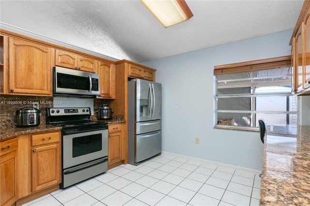 kitchen featuring a textured ceiling, light tile patterned flooring, dark stone countertops, and stainless steel appliances