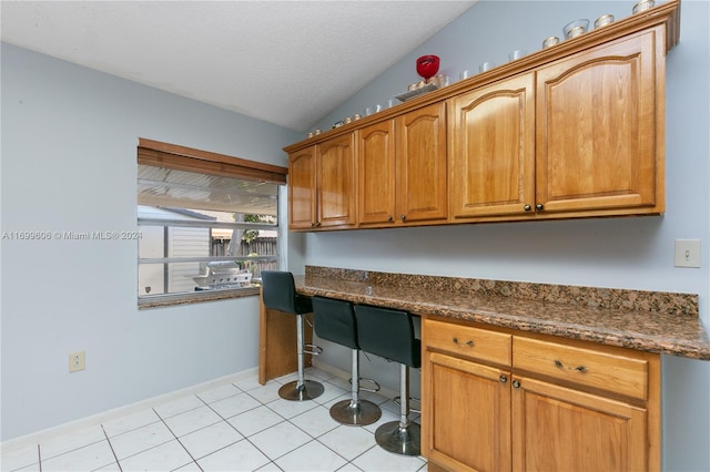 kitchen featuring light tile patterned flooring, built in desk, lofted ceiling, and dark stone countertops