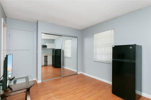 bedroom with a closet, black refrigerator, and light wood-type flooring