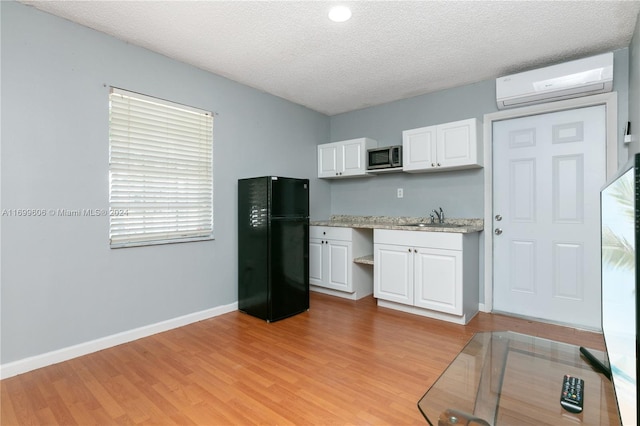 kitchen with sink, a wall mounted air conditioner, black fridge, light hardwood / wood-style floors, and white cabinets