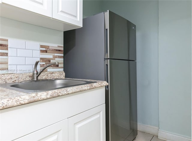 kitchen with white cabinets, refrigerator, sink, light tile patterned floors, and tasteful backsplash