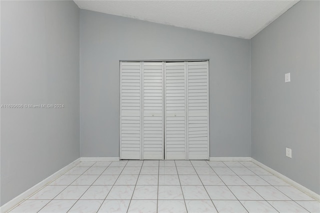 unfurnished bedroom featuring a textured ceiling, vaulted ceiling, a closet, and light tile patterned flooring