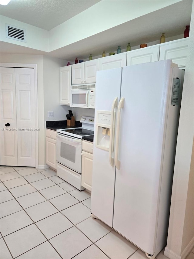 kitchen with white appliances, light tile patterned floors, dark countertops, and visible vents