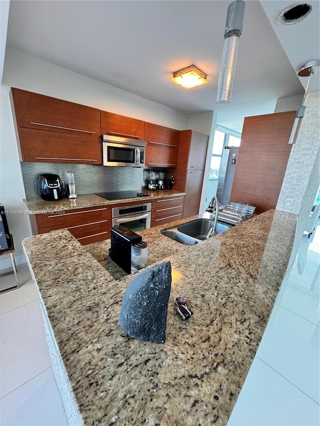 kitchen with appliances with stainless steel finishes, light stone counters, light tile patterned floors, and sink