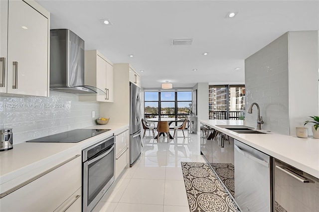 kitchen with backsplash, stainless steel appliances, sink, wall chimney range hood, and light tile patterned floors