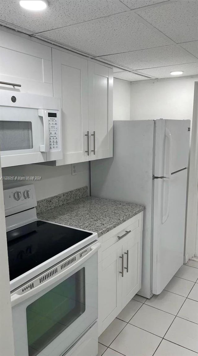 kitchen featuring white cabinets, light tile patterned floors, white appliances, and a drop ceiling