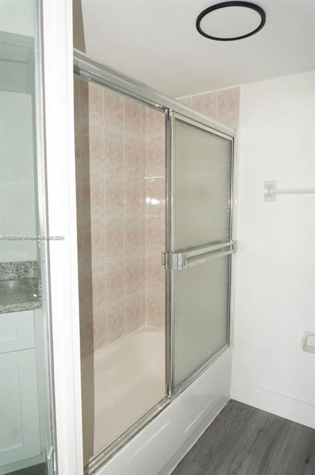 bathroom with combined bath / shower with glass door and wood-type flooring