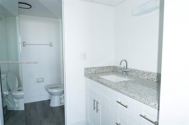 bathroom with hardwood / wood-style flooring, vanity, toilet, and an AC wall unit