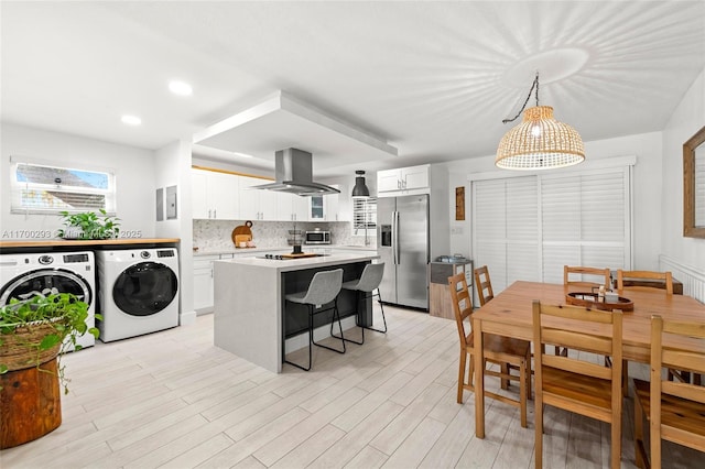 kitchen with decorative light fixtures, washing machine and clothes dryer, appliances with stainless steel finishes, white cabinets, and island range hood