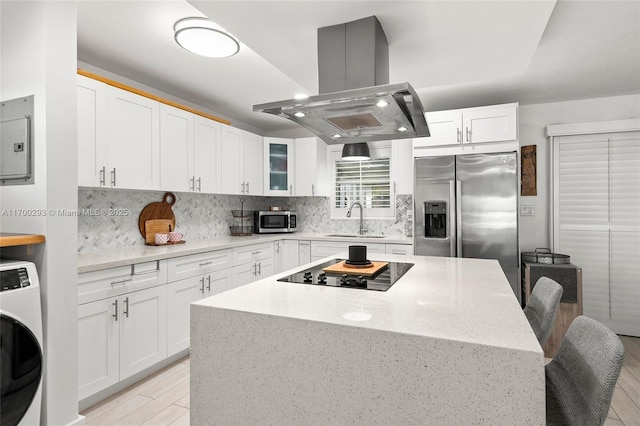 kitchen featuring washer / dryer, stainless steel appliances, white cabinets, and island exhaust hood