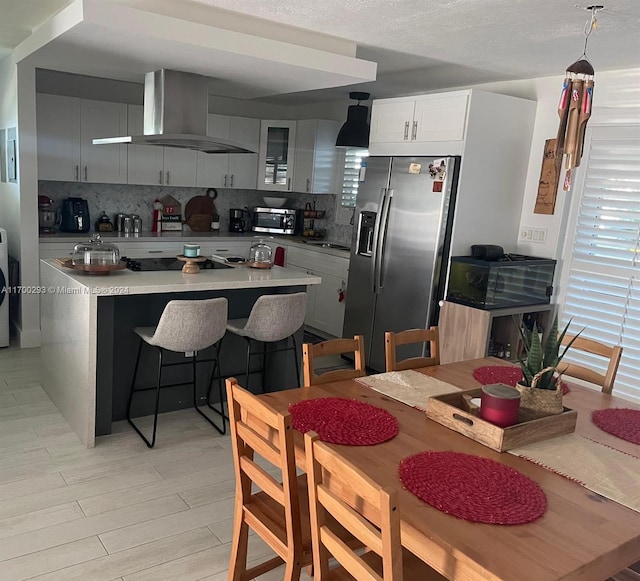 kitchen featuring wall chimney range hood, decorative light fixtures, a kitchen bar, decorative backsplash, and appliances with stainless steel finishes