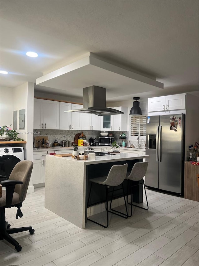 kitchen with appliances with stainless steel finishes, island range hood, white cabinets, a center island, and a breakfast bar area