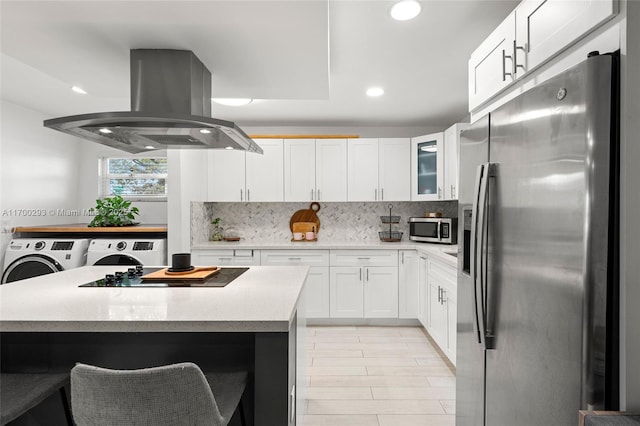 kitchen with washing machine and clothes dryer, tasteful backsplash, appliances with stainless steel finishes, white cabinets, and island exhaust hood