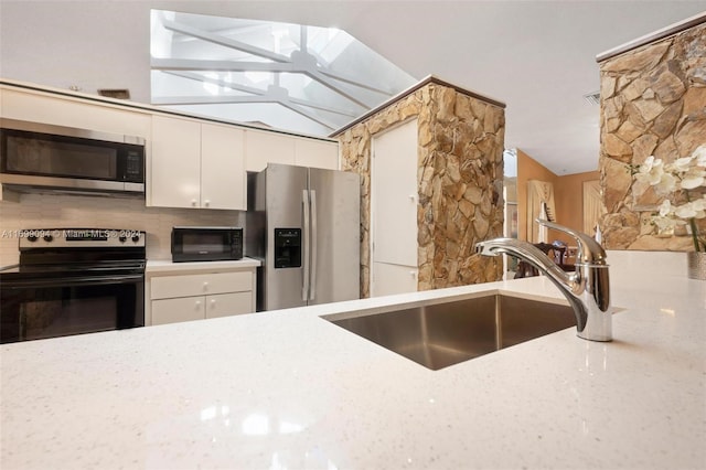 kitchen with decorative backsplash, appliances with stainless steel finishes, lofted ceiling with skylight, sink, and white cabinets