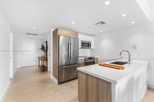 kitchen with white cabinets, appliances with stainless steel finishes, kitchen peninsula, and sink