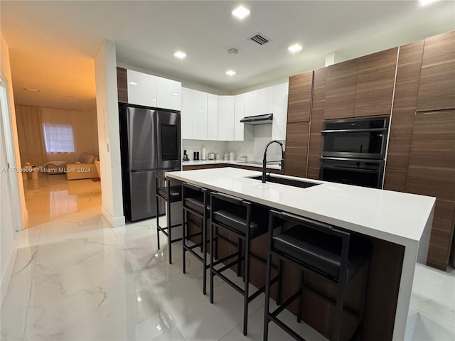 kitchen featuring sink, a kitchen breakfast bar, stainless steel fridge, black double oven, and a kitchen island with sink