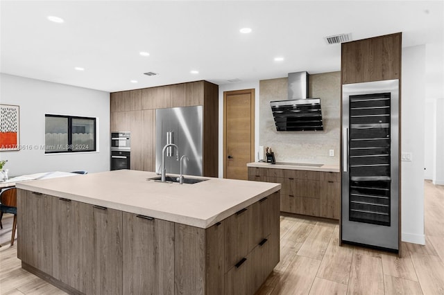 kitchen with appliances with stainless steel finishes, ventilation hood, beverage cooler, sink, and a center island with sink