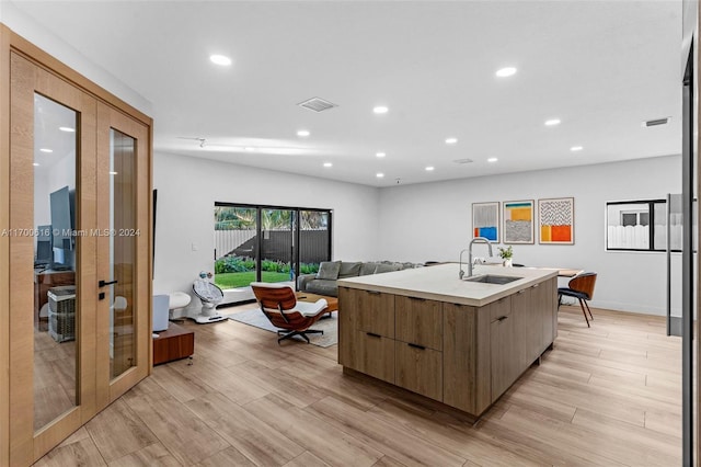 kitchen featuring french doors, sink, light hardwood / wood-style flooring, and an island with sink