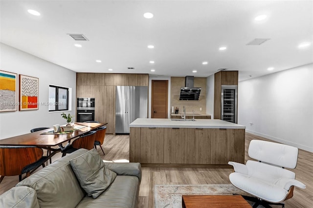 kitchen with built in fridge, a center island with sink, sink, light hardwood / wood-style flooring, and range hood