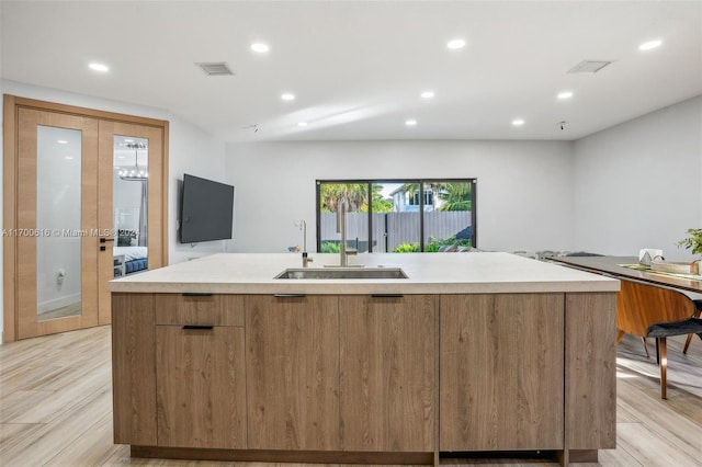 kitchen with a center island with sink, light wood-type flooring, and sink