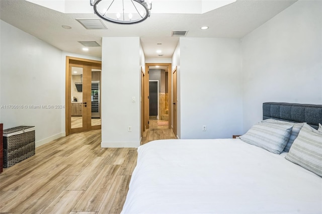 bedroom featuring ensuite bathroom, light hardwood / wood-style flooring, a textured ceiling, and a notable chandelier