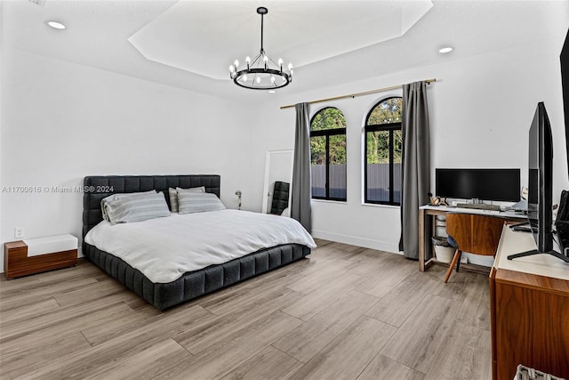 bedroom with a raised ceiling, light hardwood / wood-style flooring, and an inviting chandelier