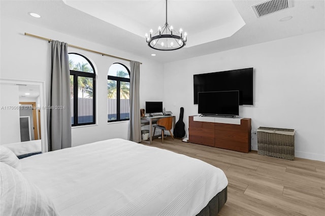 bedroom featuring a tray ceiling, light hardwood / wood-style flooring, and a chandelier