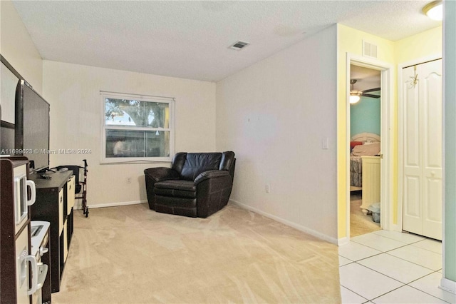 living area featuring light carpet, ceiling fan, and a textured ceiling