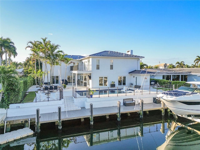 dock area featuring a water view, a patio area, a balcony, and a swimming pool