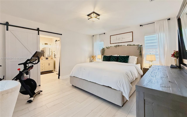 bedroom featuring ensuite bath, light wood-type flooring, multiple windows, and a barn door