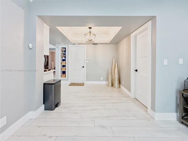 hall with a tray ceiling, built in features, and a chandelier