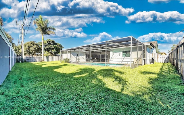 rear view of house with a lawn, glass enclosure, and a fenced in pool