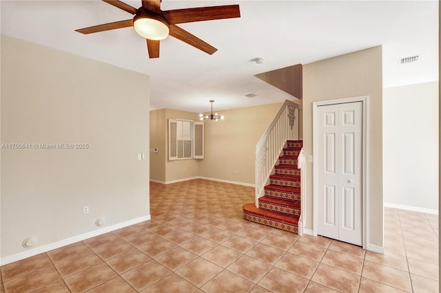 tiled empty room featuring ceiling fan with notable chandelier