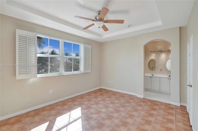 empty room with ceiling fan, a raised ceiling, sink, and light tile patterned floors