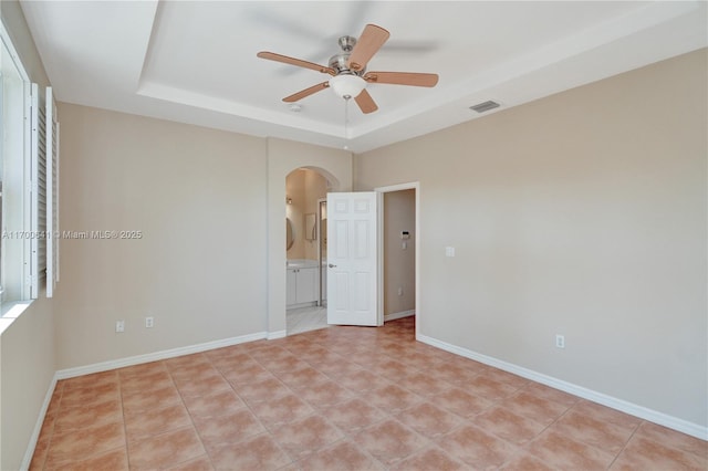 spare room with a raised ceiling, ceiling fan, and light tile patterned flooring