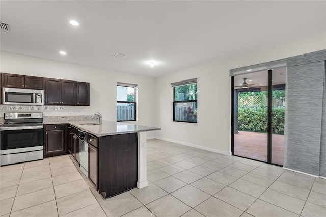 kitchen featuring kitchen peninsula, light stone countertops, stainless steel appliances, sink, and light tile patterned floors