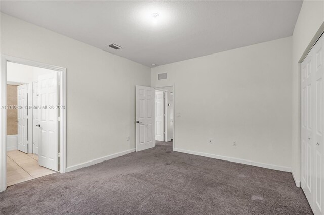 unfurnished bedroom with light colored carpet, connected bathroom, and a closet